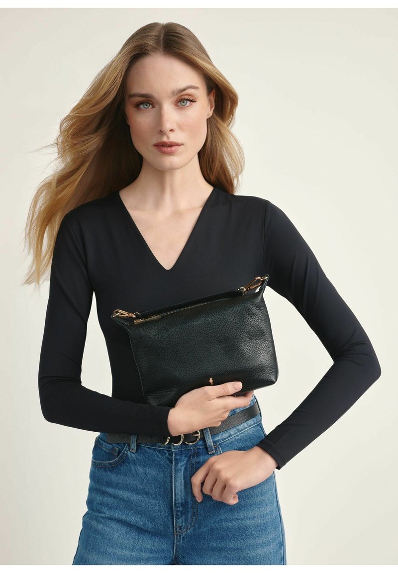 Czarna skórzana kopertówka z teksturowanym wykończeniem i złotymi detalami, trzymana przed osobą w czarnej bluzce i niebieskich dżinsach.