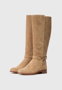 Pair of tall beige suede boots with low wooden heels and a decorative gold buckle strap around the ankle.