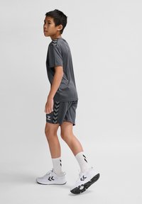 Grijze sportieve T-shirt en shorts met zwarte chevronaccenten, gecombineerd met witte sneakers en patroon-sokken. Glad, lichtgewicht stof.