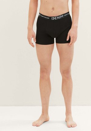 Schwarze Boxershorts mit eng anliegendem Schnitt, ausgestattet mit einem elastischen Bund, der mit "DENIM TOM TAILOR" beschriftet ist. Glattes, dehnbares Gewebe mit einer kleinen Vorderfronttasche.