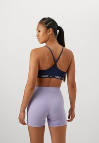 Marine sports-bh med hvit Nike-logo, med tynne stropper og ensfarget design. Lavendel høytlivshorts med en glatt tekstur og Nike-logo.