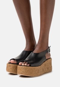Černé kožené sandály na platformě s otevřenou špičkou a náramkem kolem kotníku, s texturovaným opleteným jutovým klínem a geometrickým vzorem.