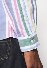 Camicia a righe multicolore con tonalità blu, rosa, verde e giallo; colletto semplice con polsini abbottonati; tessuto leggero.