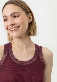 Débardeur bordeaux avec une texture côtelée et un délicat bord en dentelle le long de l'encolure et des bretelles, mettant en avant des détails de motifs complexes.