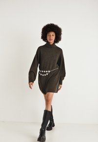 Abito maglione lavorato a maglia di colore verde scuro con collo alto, maniche ampie e finitura testurizzata, dotato di una cintura in catena argentata con accenti floreali.
