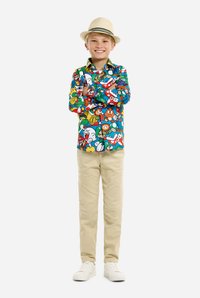 Kleurvol overhemd met cartoonfiguren, gecombineerd met khaki broek en witte sneakers. De jongen draagt een licht strooien hoed.