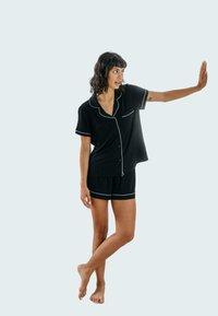 Czarny zestaw piżamowy składający się z krótkiego rękawa, zapinanego na guziki topu z białymi lamówkami oraz pasujących szortów. Miękka tkanina z luźnym krojem.