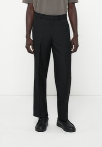 Sorte skræddersyede bukser med lige snit, knaplukning og subtil tekstur. Kombineret med sorte sneakers for et komplet look.