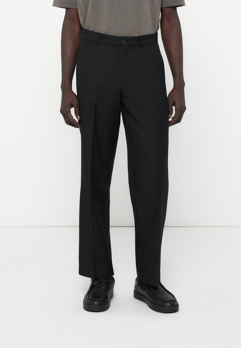 Sorte skræddersyede bukser med lige snit, knaplukning og subtil tekstur. Kombineret med sorte sneakers for et komplet look.