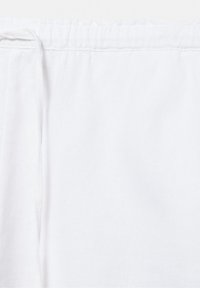 Tissu de ceinture blanche à cordon en gros plan, montrant un élastique froncé et un cordon en tissu noué sur le côté gauche.