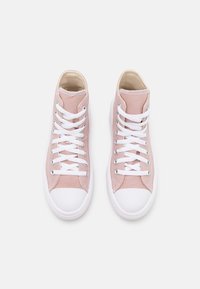 Korkea kenkämalli pehmeästä vaaleanpunaisesta kankaisesta materiaalista, jossa on valkoiset kumiset kärjet ja nauhat. Yläosassa ja kielessä on tikatussa detailia.