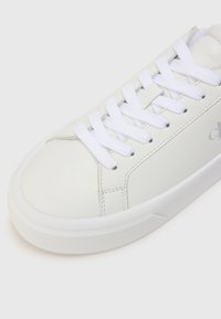 Valge nahkne toss, millel on lame valge pael, ümar varvas ja sile pind. Omab peent õmblust ja logo detaili küljel.