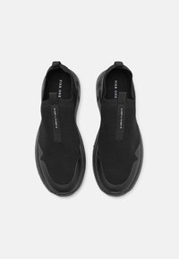 Scarpe slip-on nere con tomaia in rete, suola in gomma e linguette per una facile calzata. Texture liscia con una forma leggermente sagomata.