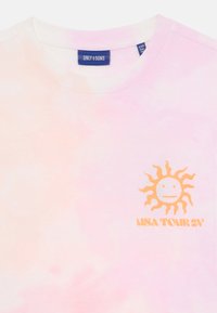 Majica s kratkimi rokavi v roza tie-dye barvi z okroglim izrezom. Ima grafiko pomarančne sončne slike in besedilo "USA TOUR 24."