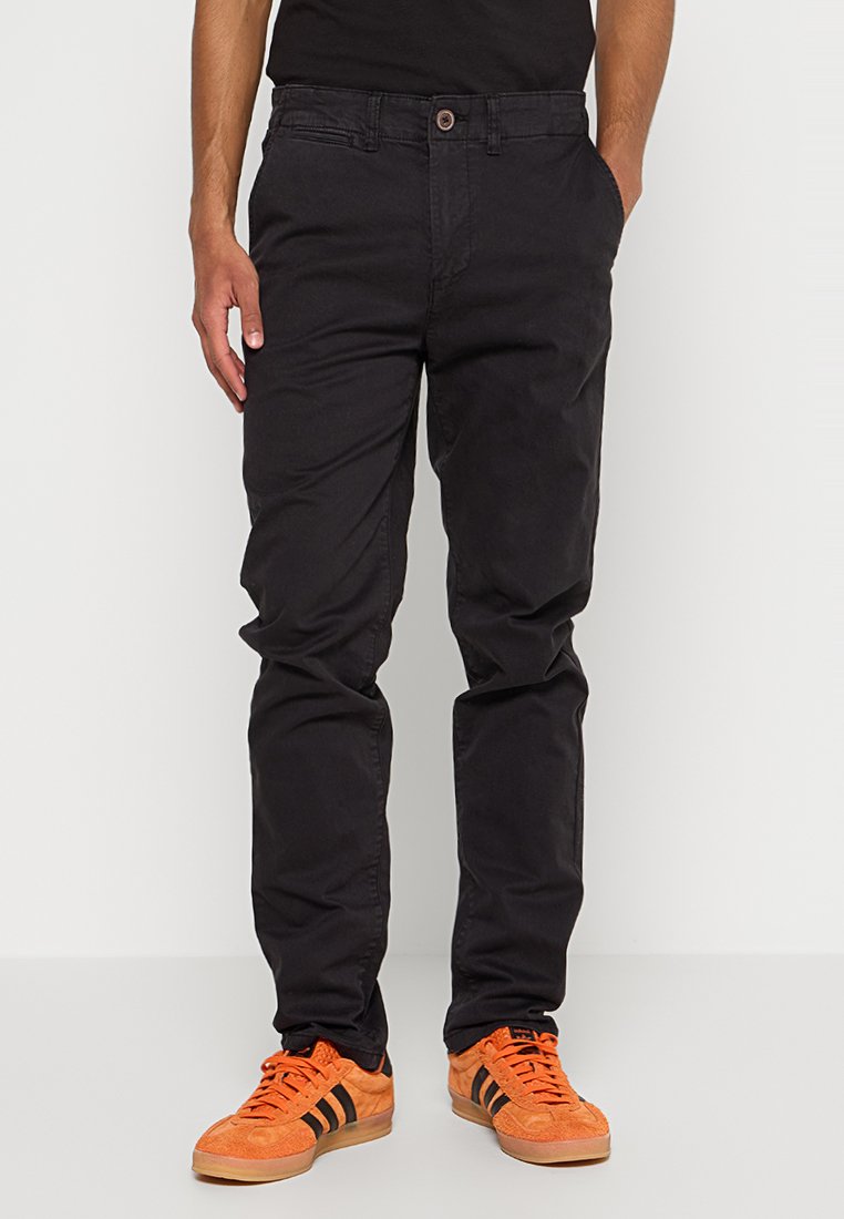 Schwarze Baumwollhosen mit geradem Bein, ausgestattet mit Fronttaschen und flachem Bund. Getragen mit orangefarbenen Sneakers.