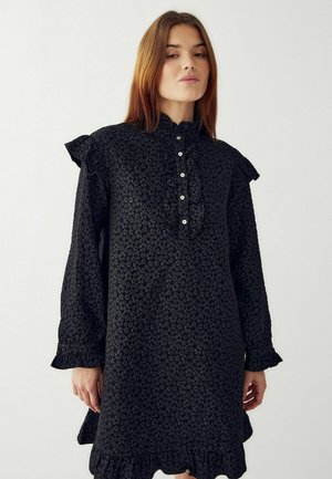 Svart blommig klänning med volangiga axlar, texturerat tyg, knäppning fram och fransad fåll. Lätt lös passform, långa ärmar.