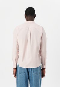 Light pink long-sleeve shirt with a button-down collar and a central pleat at the back, paired with blue denim pants.