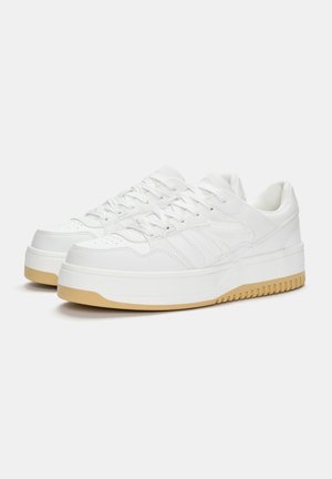 Baskets blanches en cuir texturé, avec une semelle épaisse, des accents cousus et des lacets plats. Semelle extérieure en caoutchouc de couleur beige.