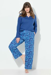 Blauwe langemouwen shirt met horizontale strepen, gecombineerd met ruime blauwe broek met een bladpatroon in verschillende tinten blauw.