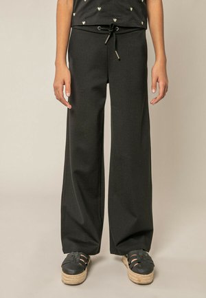 Personne portant un pantalon noir à jambes larges avec une taille à cordon et des sandales plateformes noires avec semelles tissées.