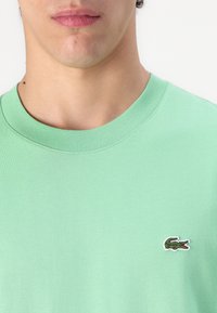 Gros plan d'une personne portant une chemise vert clair avec un petit logo crocodile brodé sur la poitrine.