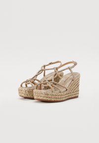 Sandales compensées avec une semelle en paille tissée, des brides en or tissées, un design à bout ouvert et un détail de nœud décoratif à l'avant.
