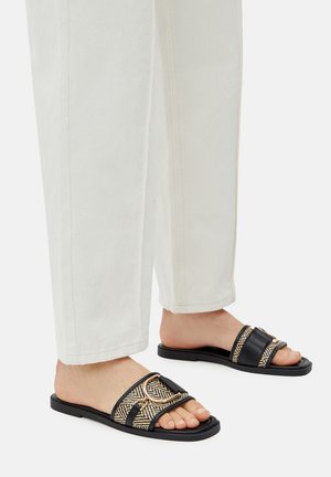 Czarno-złote klapki z wzorem plecionym i skórzanymi akcentami, wyposażone w regulowany pasek i płaskie, gumowe podeszwy.