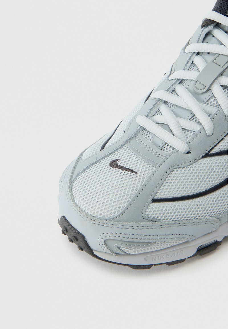 Light gray athletic shoe with mesh upper, white laces, subtle black accents, rounded toe, and textured rubber sole. Features Nike logo.