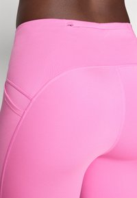 Rosa høye leggings laget av elastisk materiale med buede sømmer og en glidelåslomme på baksiden for praktisk bruk og passform.