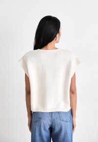 Short-sleeve, cream knit top with a rounded neckline, ribbed hem, and smooth texture, paired with blue denim jeans.