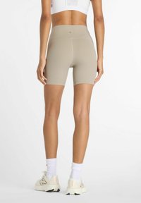 Shorts de vélo taille haute en beige clair, avec un design sans coutures et une marque discrète. Portés avec des baskets blanches et des chaussettes.