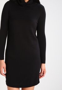 Abito nero a maniche lunghe realizzato in tessuto morbido con scollatura a cappuccio. Il design è aderente con orlo dritto e senza motivi o dettagli visibili.
