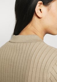 Maglione a coste beige con colletto, tessuto testurizzato e silhouette aderente, che enfatizza i motivi e i dettagli sottili.