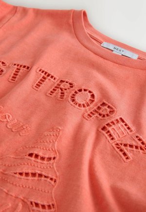 Koralinė džemperio su išpjautomis raidėmis ir siuvinėtais akcentais. Lygus medvilnės audinys su ribotu apvaliu kaklu ir minkšta tekstūra.