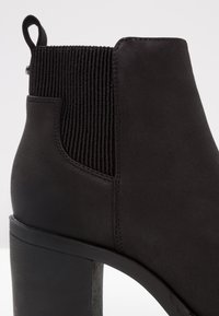 Stivale ankle nero con finitura in camoscio, pannelli laterali elasticizzati e tacco cilindrico testurizzato. Il design presenta dettagli di cucitura minimi.