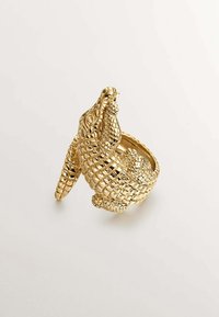 Anillo de color dorado con un diseño detallado de cocodrilo, que muestra un acabado texturizado y escamoso, con un acento de cola rizada.