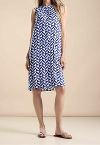 Modrá a bílá geometricky vzorovaná bezramínková šaty se skládáním u výstřihu, kratší délka ke kolenům a volný střih. Měkká struktura tkaniny.