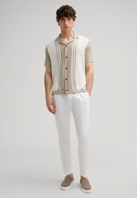 Men's short-sleeve button-up shirt in cream and beige with vertical stripes. Paired with white trousers and beige slip-on shoes.