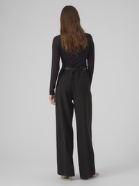 Schwarzes langärmliges Oberteil kombiniert mit schwarzer Hose mit weitem Bein. Das Oberteil ist figurbetont geschnitten, während die Hose eine hohe Taille und eine fließende Silhouette aufweist.