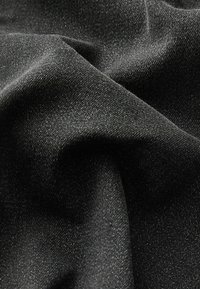 Czarna tkanina dżinsowa o gładkiej teksturze, delikatnym połysku i subtelnych zróżnicowaniach splotu, ukazująca miękkie układanie się i zagniecenia.