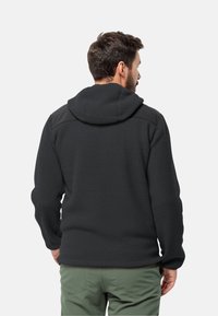 Giacca in pile nera con superficie testurizzata, cappuccio e accenti neri a contrasto sulle spalle. Presenta una tasca con zipper di lato.