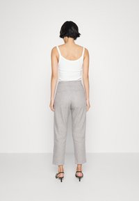 Vit ärmlös topp i kombination med ljusgrå högmidjade byxor. Byxorna har en rak passform och subtilt strukturerad tyg, bärs med svarta klackskor.