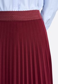 Falda burgundy plisada con una cinturilla fruncida texturizada. El material parece suave con pliegues verticales distintos.