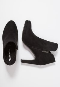 Schwarze Wildleder-Stiefeletten mit hohen Absätzen, ausgestattet mit einem seitlichen Reißverschluss und einem runden Zehenbereich. Glatte Oberfläche und minimalistischer Stil.