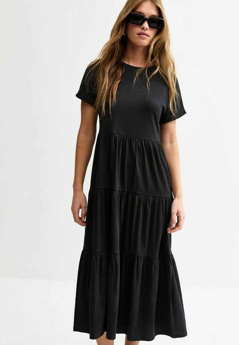 Vestido midi negro con capas, hecho de una tela suave, que cuenta con mangas cortas y un corte relajado con un dobladillo inferior fluido.