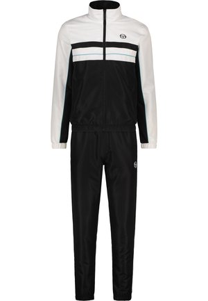 Tuta bianco e nero realizzata in tessuto liscio; presenta una giacca con zip con strisce e logo, e pantaloni abbinati elasticizzati.