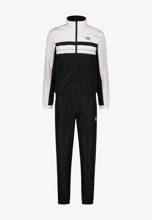 Tuta bianco e nero realizzata in tessuto liscio; presenta una giacca con zip con strisce e logo, e pantaloni abbinati elasticizzati.