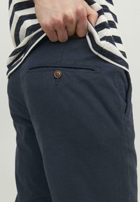 Marinefarbene Hose mit glatter Textur, ausgestattet mit einer Gesäßtasche, runder Knopfverschluss und einem dezenten diagonalen Webmuster.