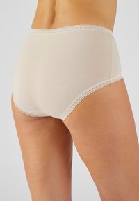 Culotte en coton beige avec une texture lisse, ornée de délicates bordures en dentelle le long de la ceinture et des ouvertures de jambes pour plus de détails et de confort.