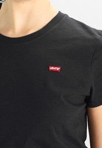 Czarny bawełniany t-shirt z okrągłym dekoltem i krótkimi rękawami. Posiada czerwoną naszywkę z logo Levi's na piersi. Gładka struktura.